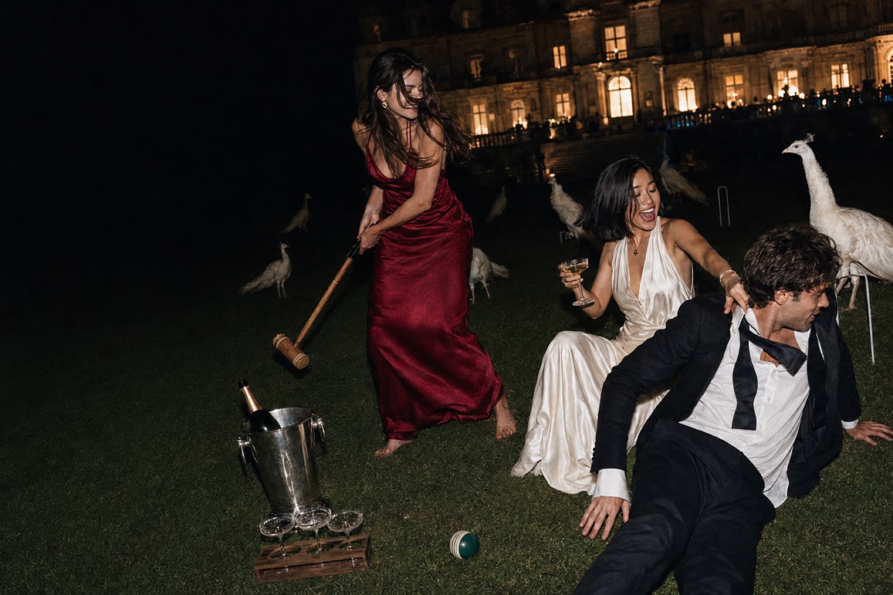 A croquet game played by lamplight on a manicured lawn at night